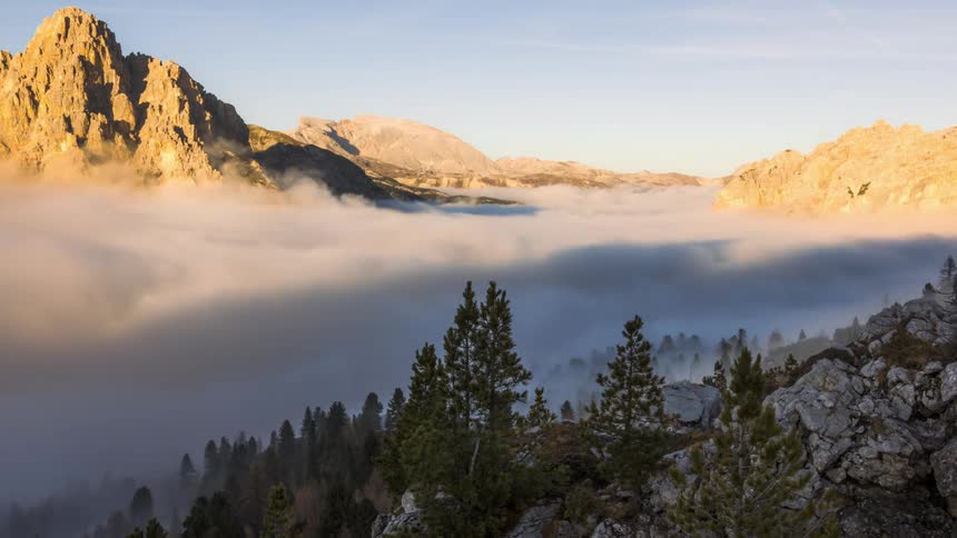 Thickening fog obscures forest in the valley between craggy mountains