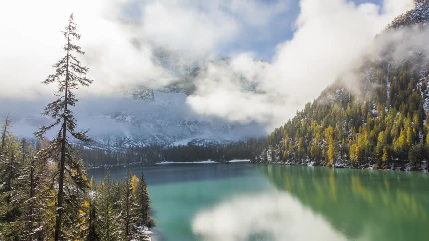 Tranquil lake surrounded by trees and mountains in the background under a partly cloudy sky
