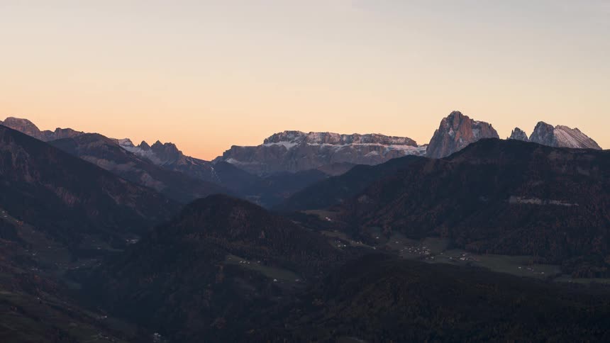 Snow dusted mountains under a bright sky that turns to night