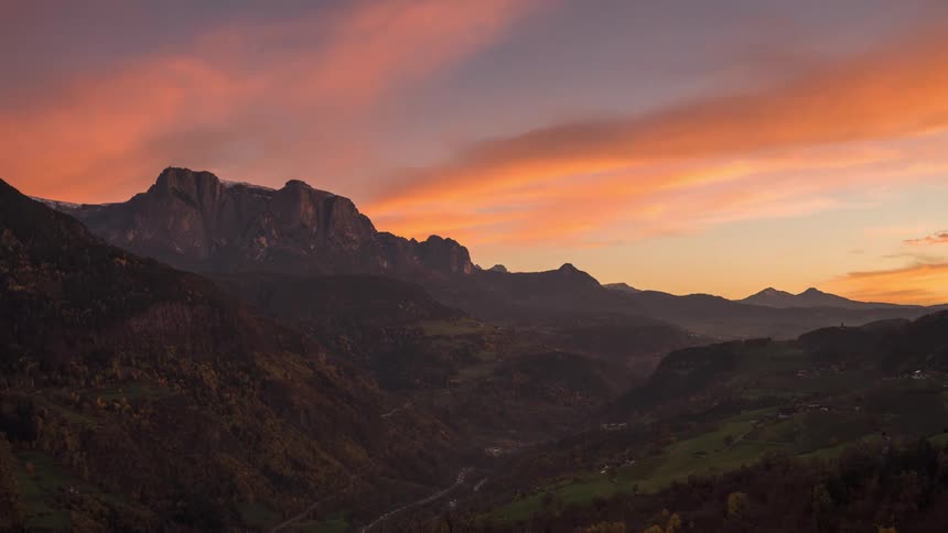 Cars drive around a mountain valley as dark storms pass overhead