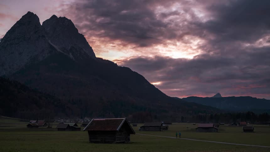 People walk and cars drive around a rural community sitting in a mountain valley as dark clouds move overhead