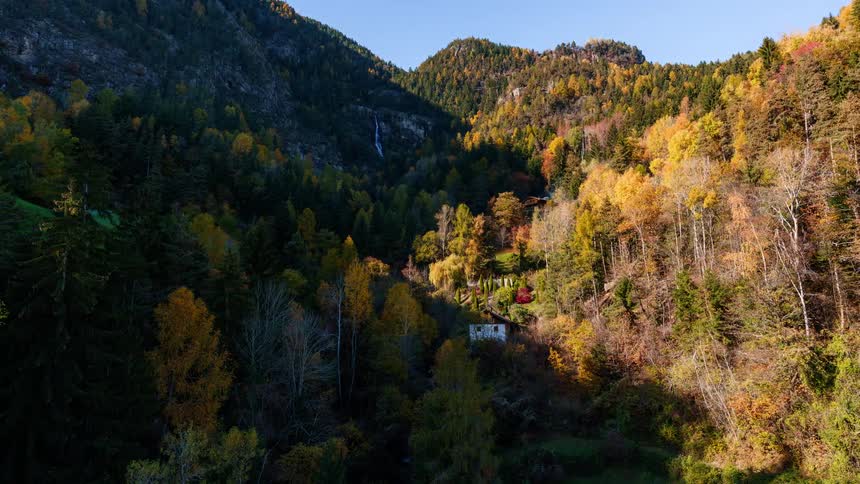 A small white house sits in a forested mountain valley