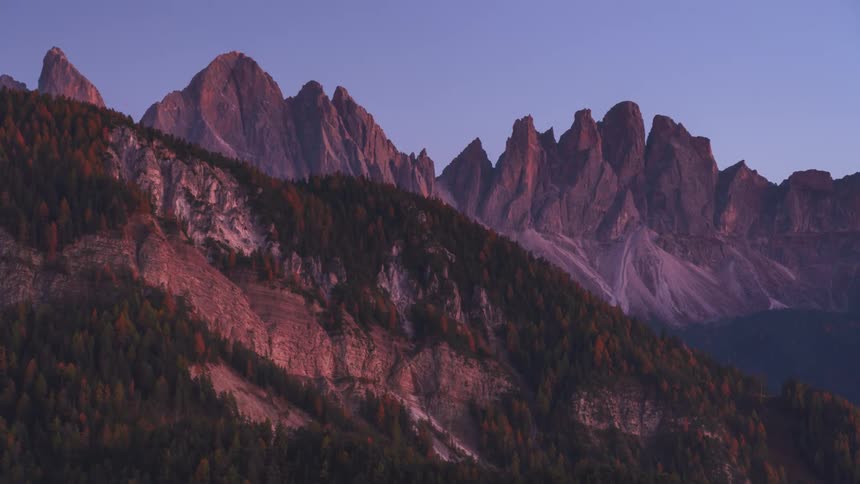 Mountain range at twilight with sharp peaks and steep slopes bathed in soft purples and blues