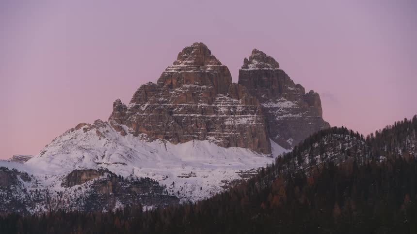 Mountains with conifers and snow and the reflection of sunlight fading at dusk