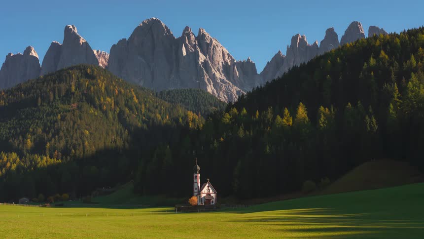 Tall craggy mountains tower over forested mountains bordering a religious building