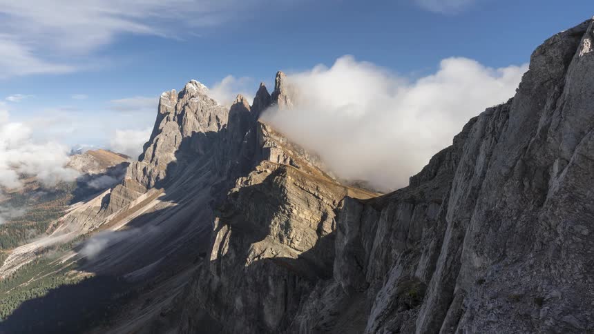 Clouds flow over mountains towering over forest on a cloudy day
