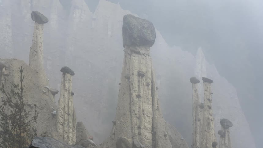 Fog grows denser obscuring cliff and forest behind tall narrow rock formations