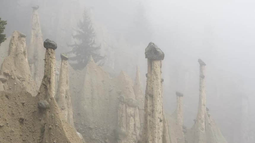 Several tall narrow rock formations with rounded tops that seem to balance larger rocks surrounded by fog
