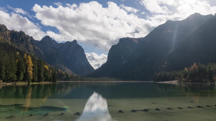 Natural landscape of a calm lake surrounded by wooded mountains during blue sky day with clouds