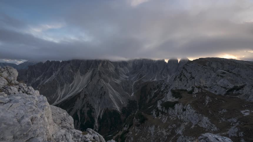 Clouds cover the setting sun as it goes behind rocky mountains