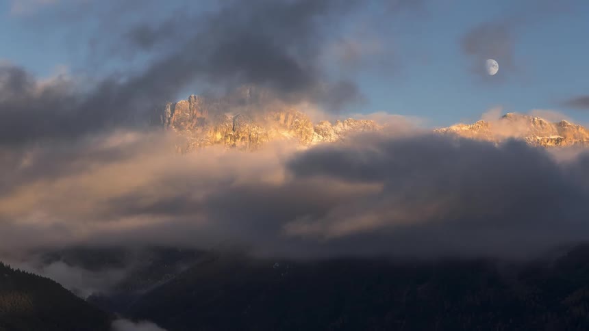Mountainous landscape with snowcapped peaks and low clouds illuminated by the setting sun