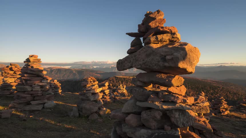 Several piles of rocks carefully balanced on top of each other in the foreground with a mountainous horizon in the background under a clear evening sky