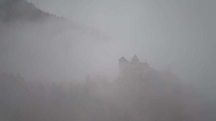 Castle shrouded in dense fog with trees around