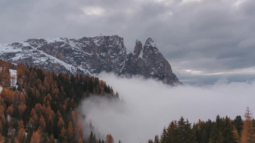 Snowy mountains landscape with autumn conifers around with low clouds