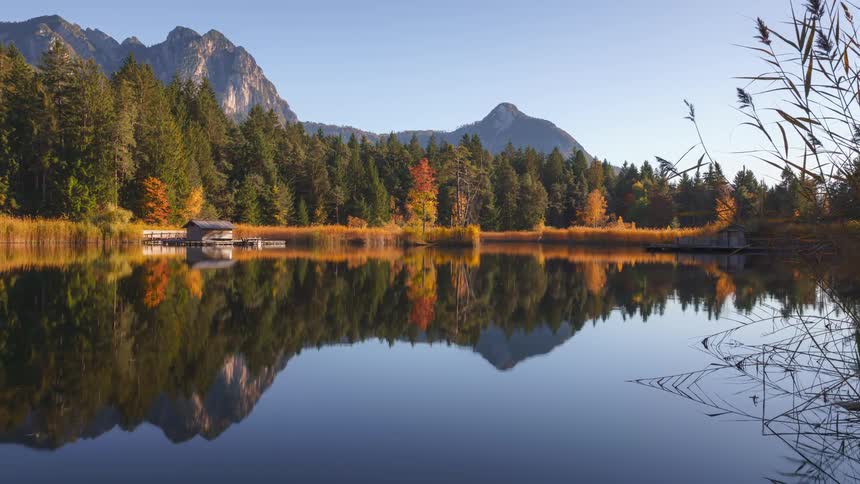 Tranquil lake reflecting shore with conifers against a blue sky