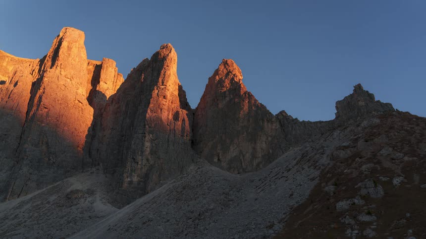 Time lapse of sunset falling over a rugged mountain landscape under a clear blue sky