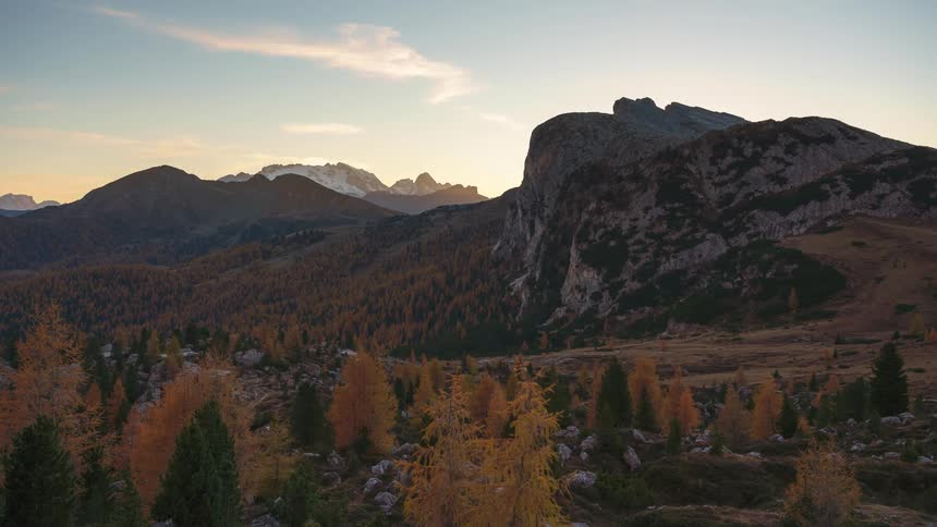 The sun peeks over a mountain summit beside a forest