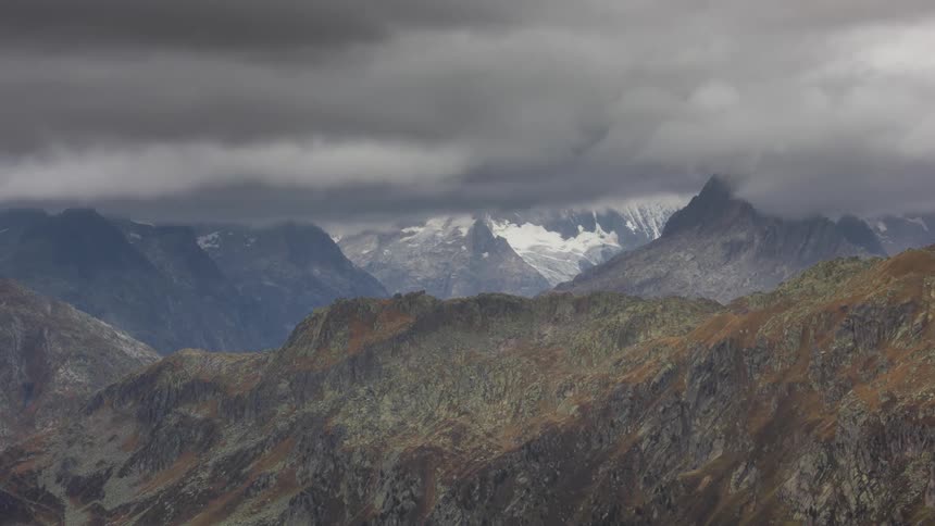 A mountainous landscape with rocky peaks under a rapidly moving cloudy sky