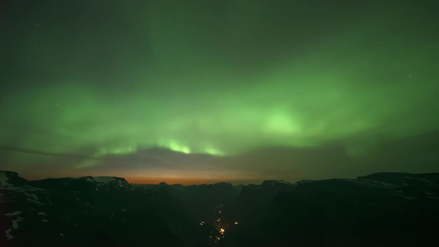 Night landscape of greenish northern lights above mountain silhouettes
