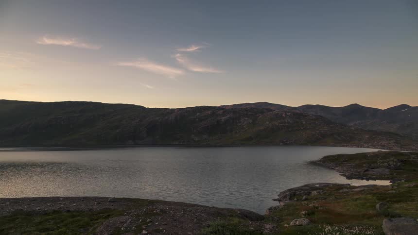 Lake surrounded by mountains with a dusk and clouds passing by