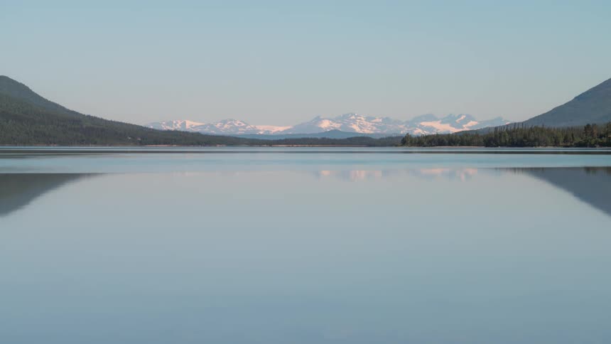 Large calm lake against a dawn sky and with snowcapped mountains on the horizon