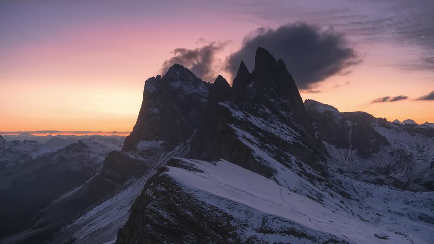 Clouds flow over snow covered mountain range during as sunrise turns into day
