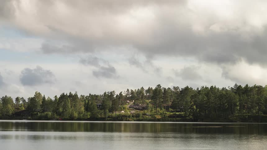 Dark and white clouds billow over buildings in a rural area situated near a lake shore