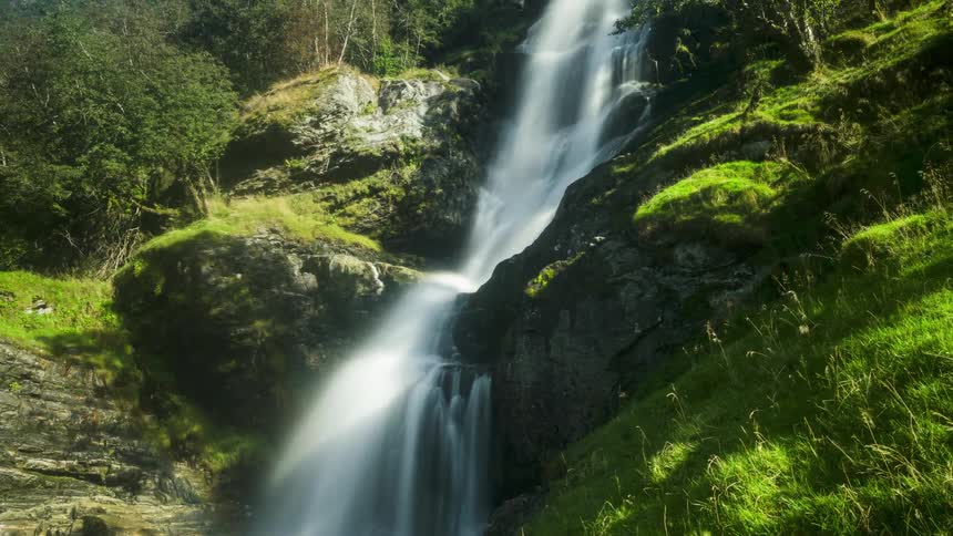 A cascading waterfall plunges into a lush green forest