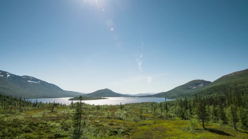 Mountains and woods surround lake reflecting the shifting sun