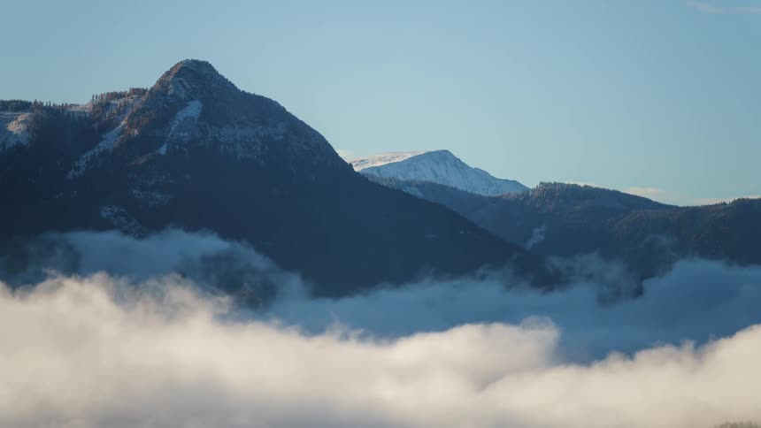 Clouds roll near the mountain peaks under a clear blue sky