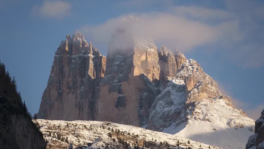 Mountains with rocky peaks and snowcapped cliffs against a partly cloudy blue sky