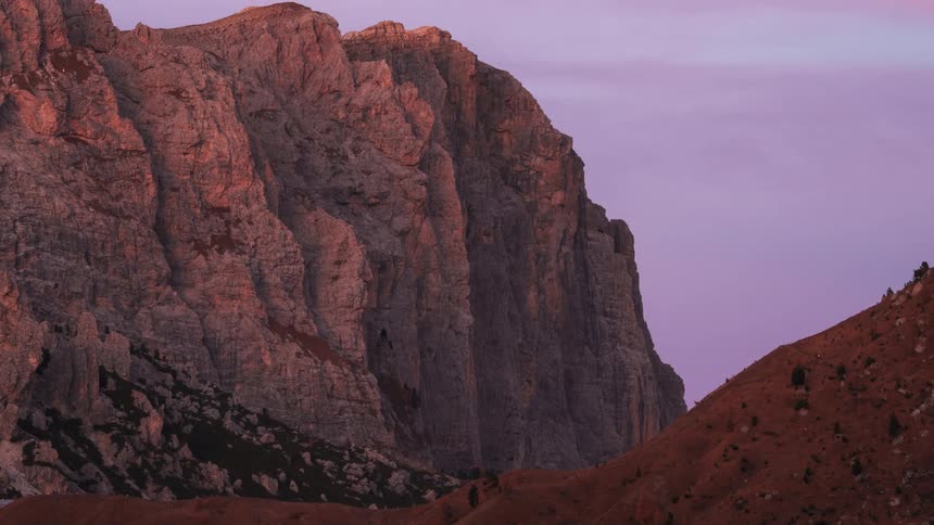 Red sunlight fades on the surface of a cliff towering over a hill