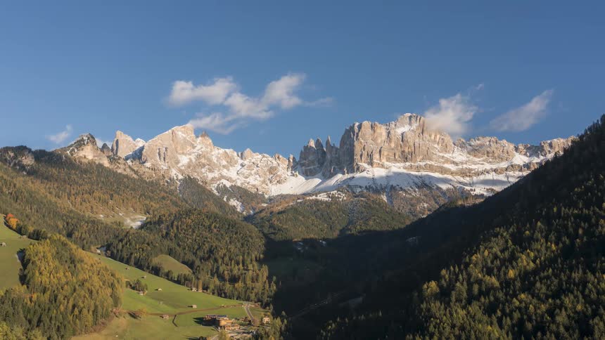 Aerial scenery of greenish mountains with snowy trees and cliffs on the horizon against a blue sky with low clouds