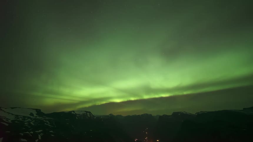 Time lapse of aurora lights shining brightly across the sky in the mountains