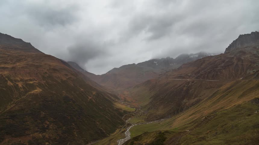 White and gray clouds flow over the mountains that are divided by a river