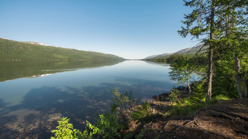 Calm lake reflecting the mountainous edges against a blue sky