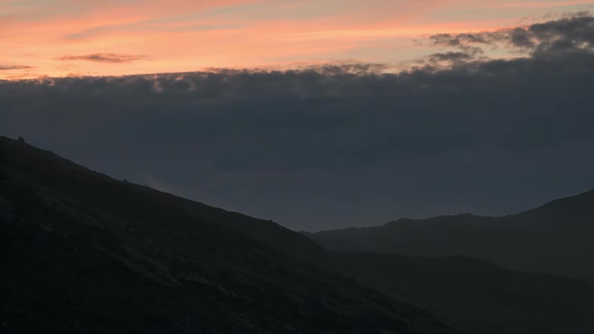 Thick clouds rise over mountains at sunset