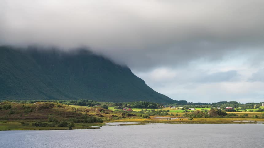 Low dense clouds passing above greenish mountains on the edge of a lake