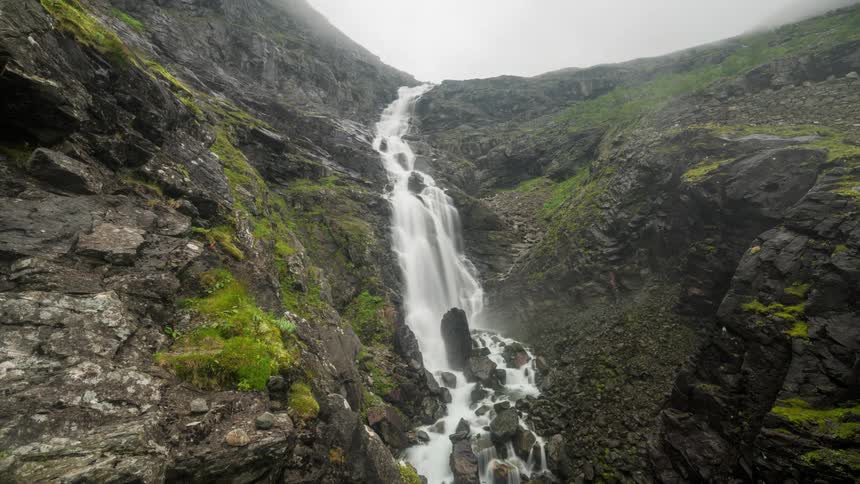 Time lapse of a water fall flowing down a grassy cliff to rocks below