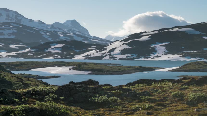 Snowcapped mountains rapidly moving clouds a serene blue lake and lush green vegetation