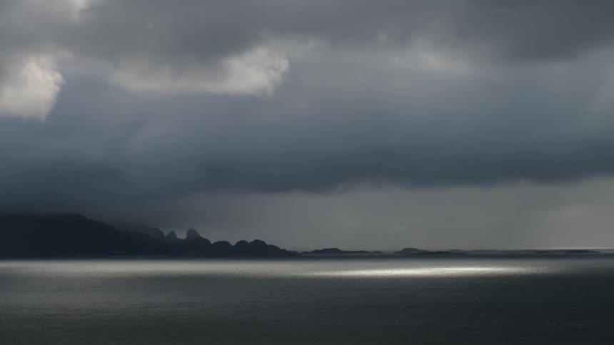 The sun shines through dark clouds over an ocean
