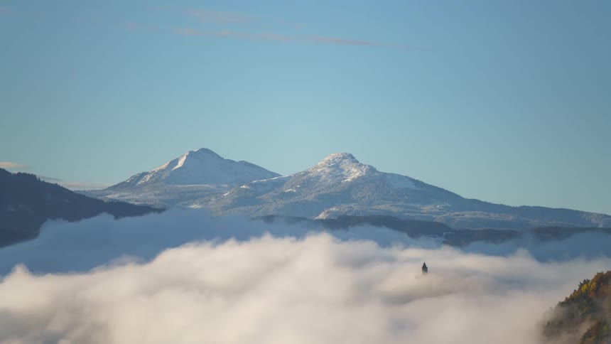 Seascape of low clouds passing through snowy mountains against a blue sky