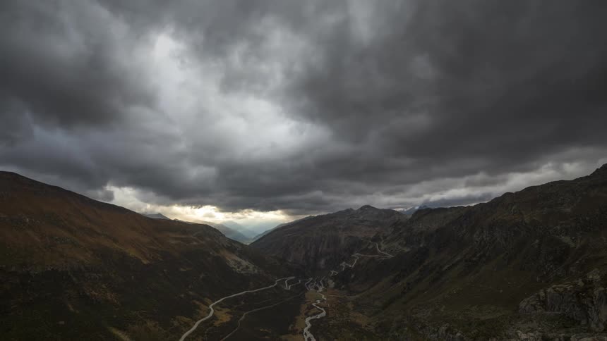Grey storm clouds loom over a ravine in a mountain range in a timelapse video