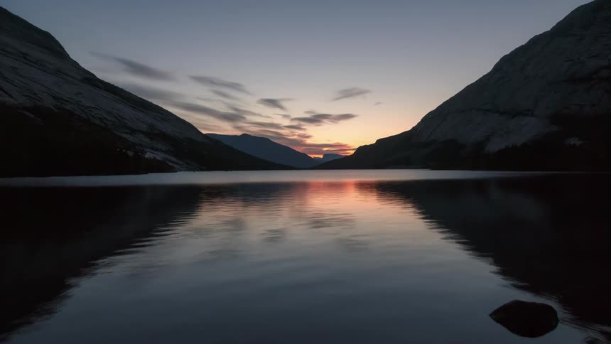 Time lapse of clouds rolling over a lake in the mountains at sunrise