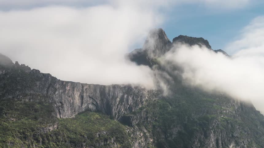Time lapse of clouds rolling over green mountains under a blue sky