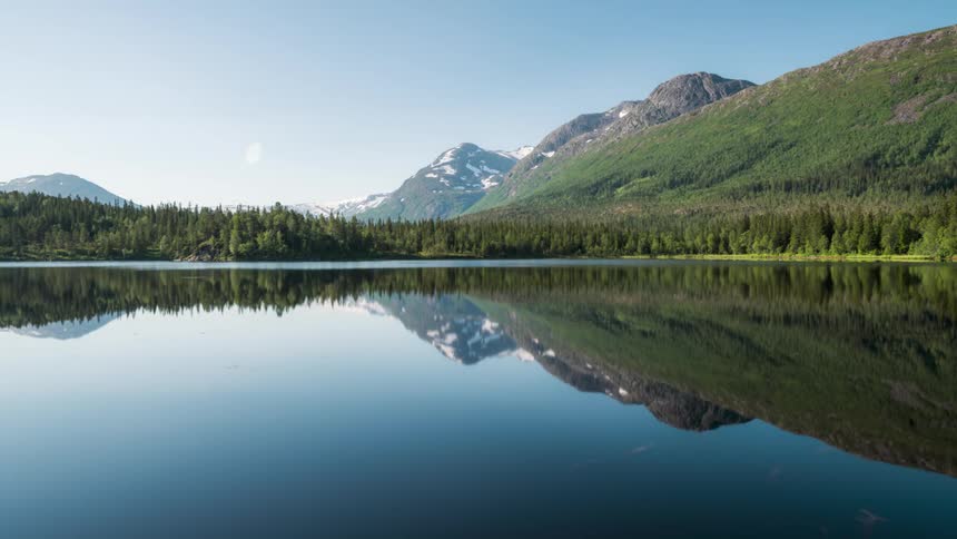 A serene lake reflects the snowcapped mountains in the distance