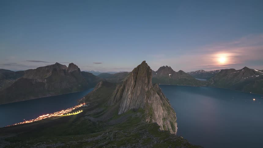 He colorful ribbons of the aurora borealis dance across the night sky above a coastal town anda snowcapped mountain range