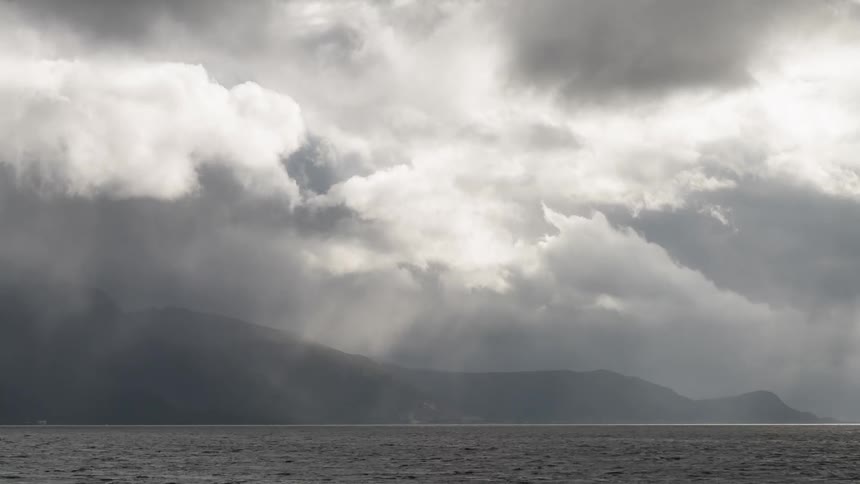 A big storm moves over mountains and a coast as a boat chugs to shore