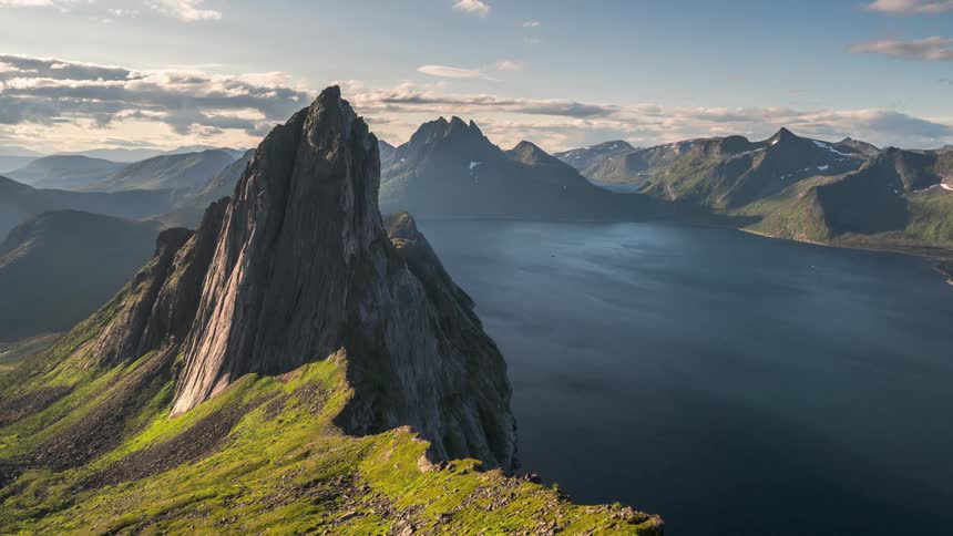 Mist flows between mountain peaks under a partly cloudy sky