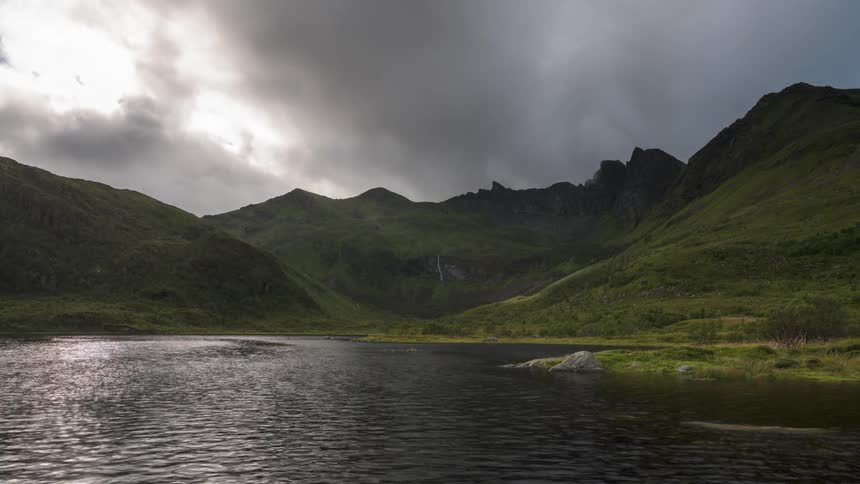 Dark clouds pour over a mountain range and move over a lake shore